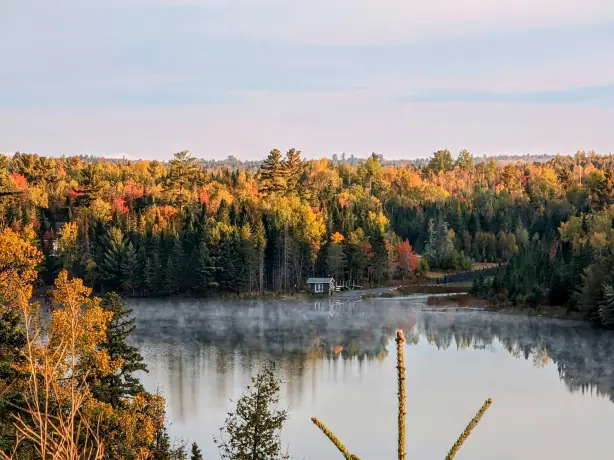 Am Ufer eines Sees, umgeben von einem farbenprächtigen Herbstwald, steht eine kleine Hütte