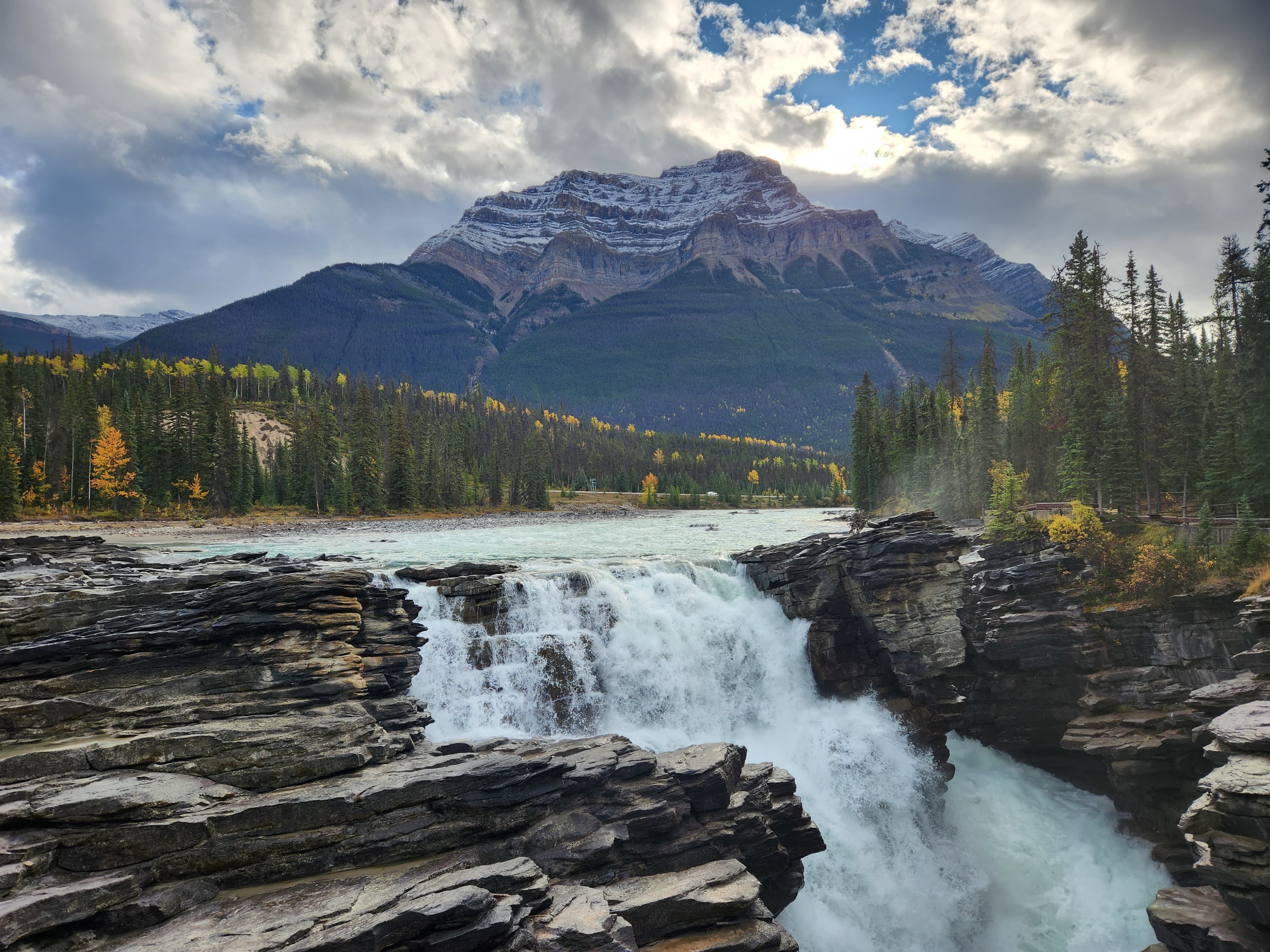 A river flows into a cascade with trees and mountains in the background in Banff National Park, Canada