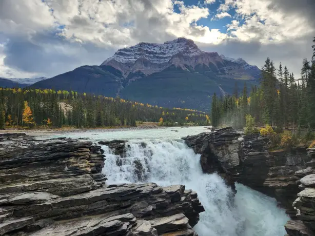 A river flows into a cascade with trees and mountains in the background in Banff National Park, Canada