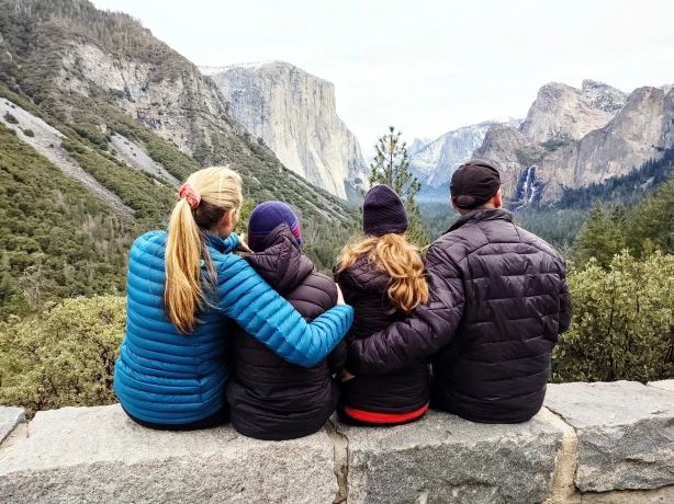 Eine vierköpfige Familie sitzt gemeinsam auf einer Mauer im Yosemite-Nationalpark und genießt den Blick auf hoch aufragende Granitfelsen und Wasserfälle