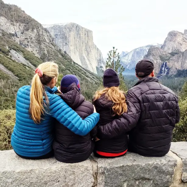 Eine vierköpfige Familie sitzt gemeinsam auf einer Mauer im Yosemite-Nationalpark und genießt den Blick auf hoch aufragende Granitfelsen und Wasserfälle
