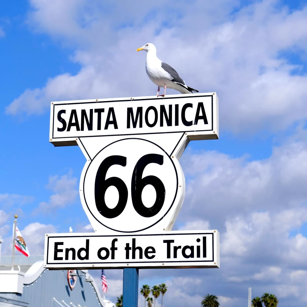 Das "End of the Trail"-Schild der Route 66 in Santa Monica, USA, mit einer Möwe, die vor einem strahlend blauen Himmel auf dem Schild thront.