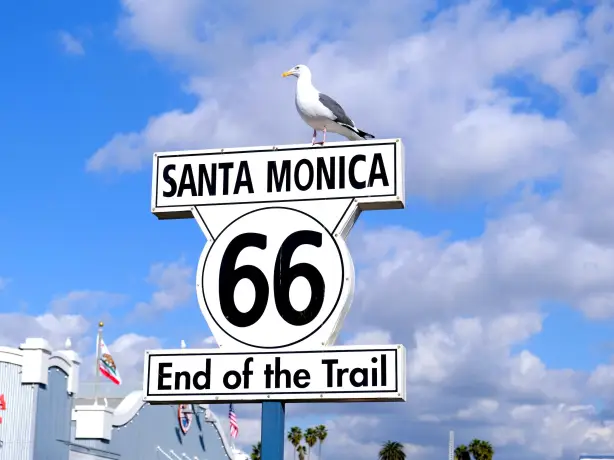 Das "End of the Trail"-Schild der Route 66 in Santa Monica, USA, mit einer Möwe, die vor einem strahlend blauen Himmel auf dem Schild thront.