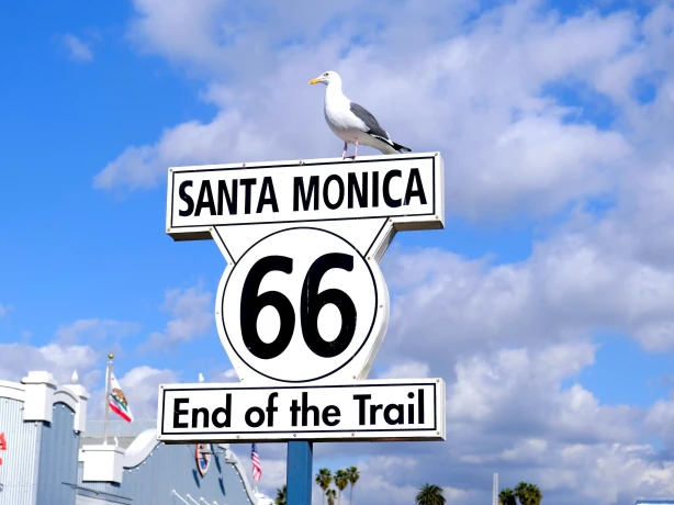Das "End of the Trail"-Schild der Route 66 in Santa Monica, USA, mit einer Möwe, die vor einem strahlend blauen Himmel auf dem Schild thront.