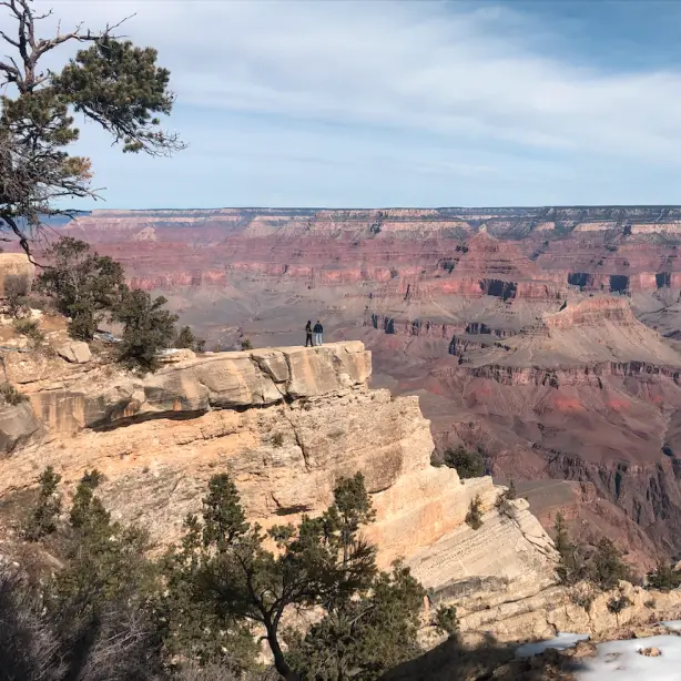 Zwei Menschen stehen am Rand eines Kraters und blicken über den Grand Canyon in Arizona.