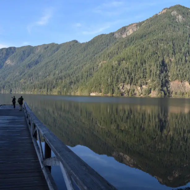 Een houten steiger die uitkijkt over een helder meer met beboste bergen op de achtergrond