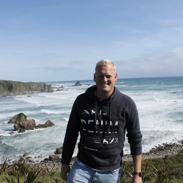 Maurits glimlacht naar de camera met de oceaan op de achtergrond