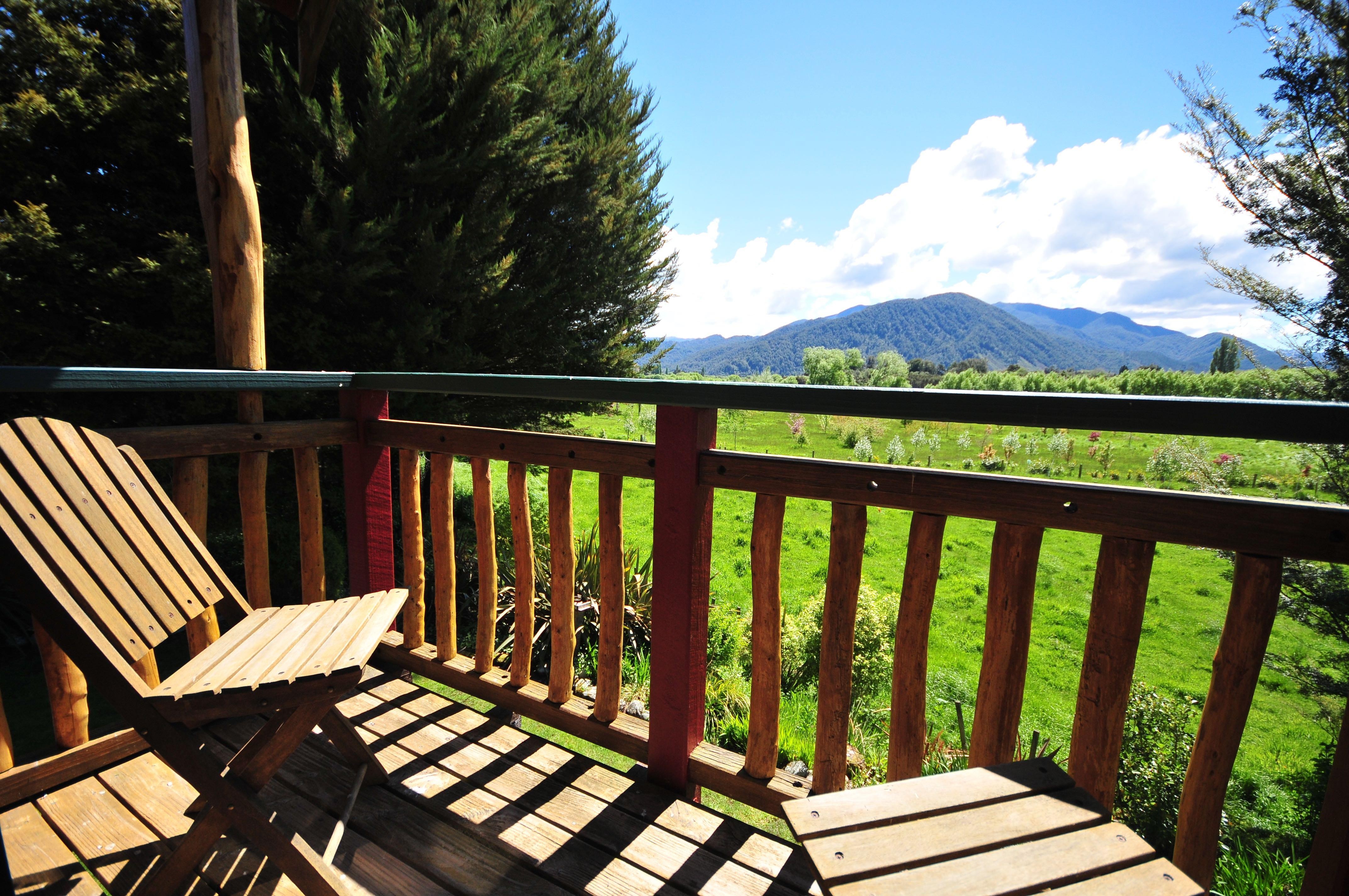 Blick auf die Berge über die grüne Wiese von der hölzernen Veranda mit Sitzgelegenheiten