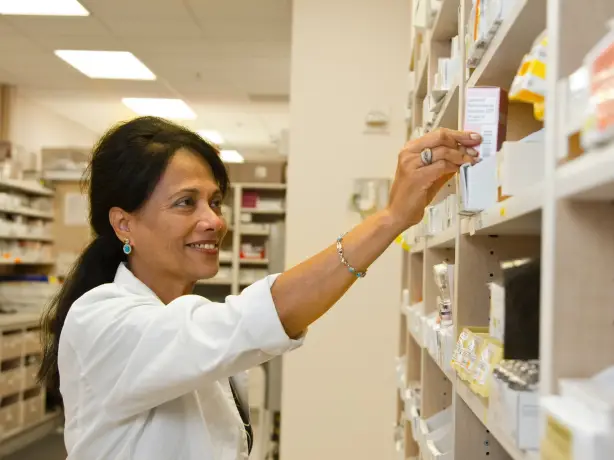 Apothekerin nimmt Medikament aus einem Regal in der Apotheke