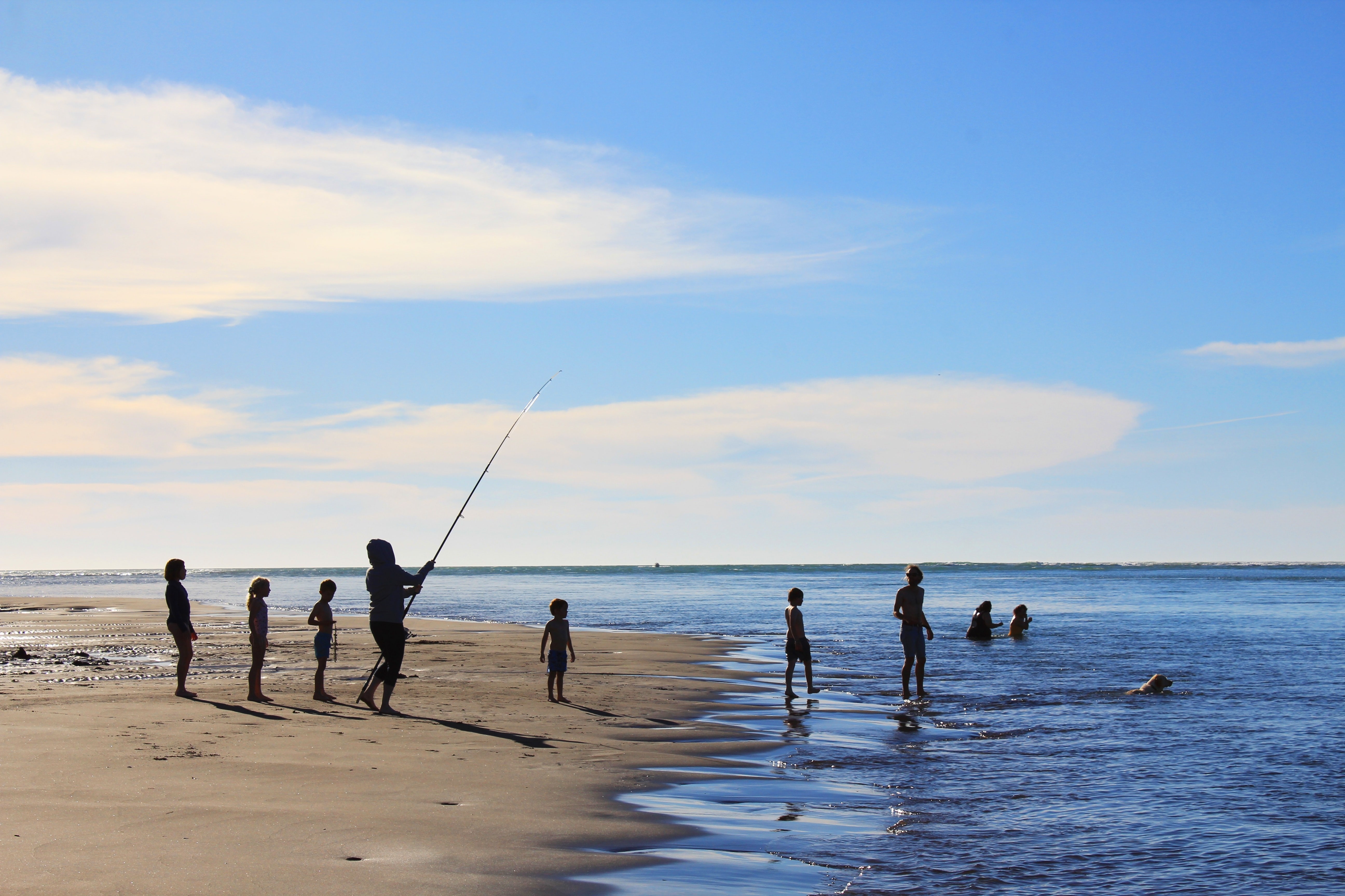 Personen stehen an Strand und angeln in Neuseeland
