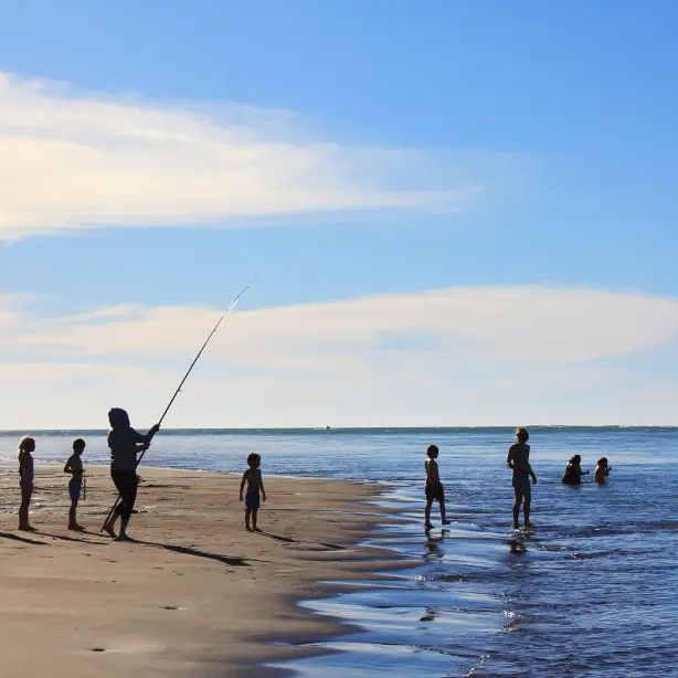 Personen stehen an Strand und angeln in Neuseeland