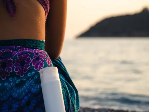 Frau von hinten, die auf Kieselstrand und Gewässer sitzt mit einer Sprayflasche an ihr gelehnt