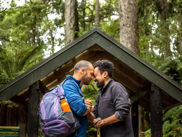 Zwei Männer führen einen traditionellen Māori-Gruß in einem Wald auf.