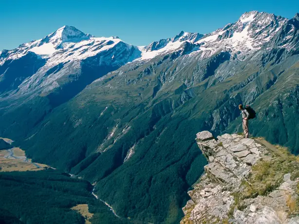 Wanderer steht auf Felsvorsprung mit schneebedeckten Bergen im Hintergrund