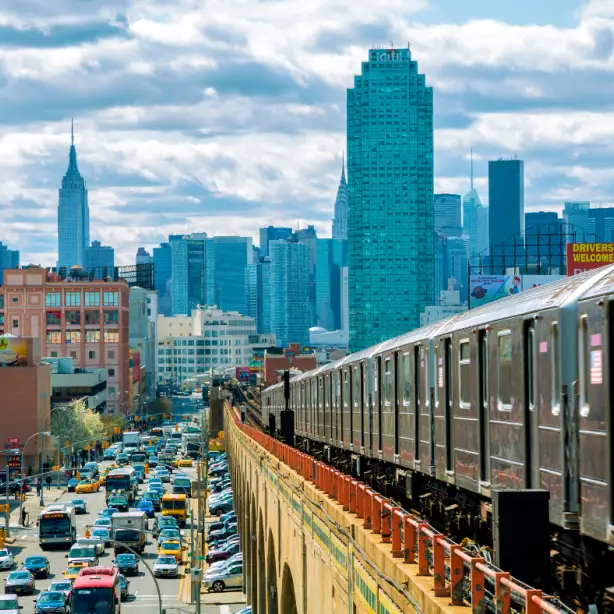 Een tram rijdt op een verhoogde brug met uitzicht op de skyline van Queens