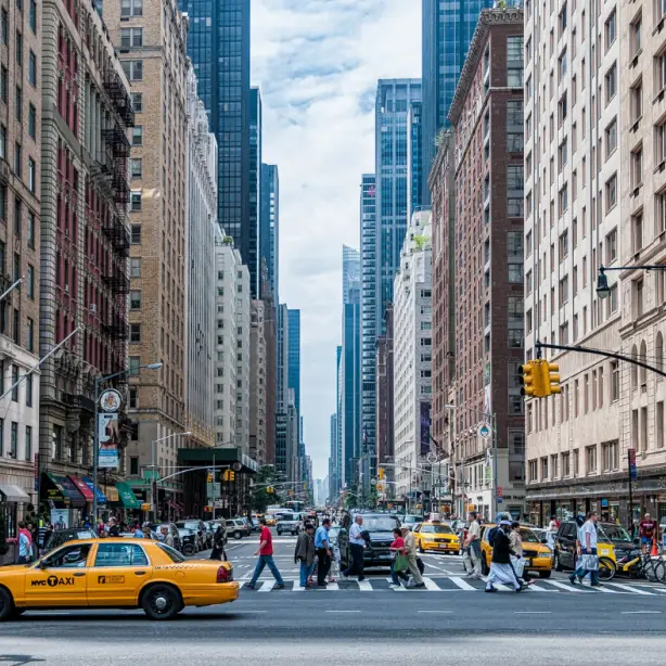 Een straat in New York, mensen steken een zebra over en er rijdt een gele taxi