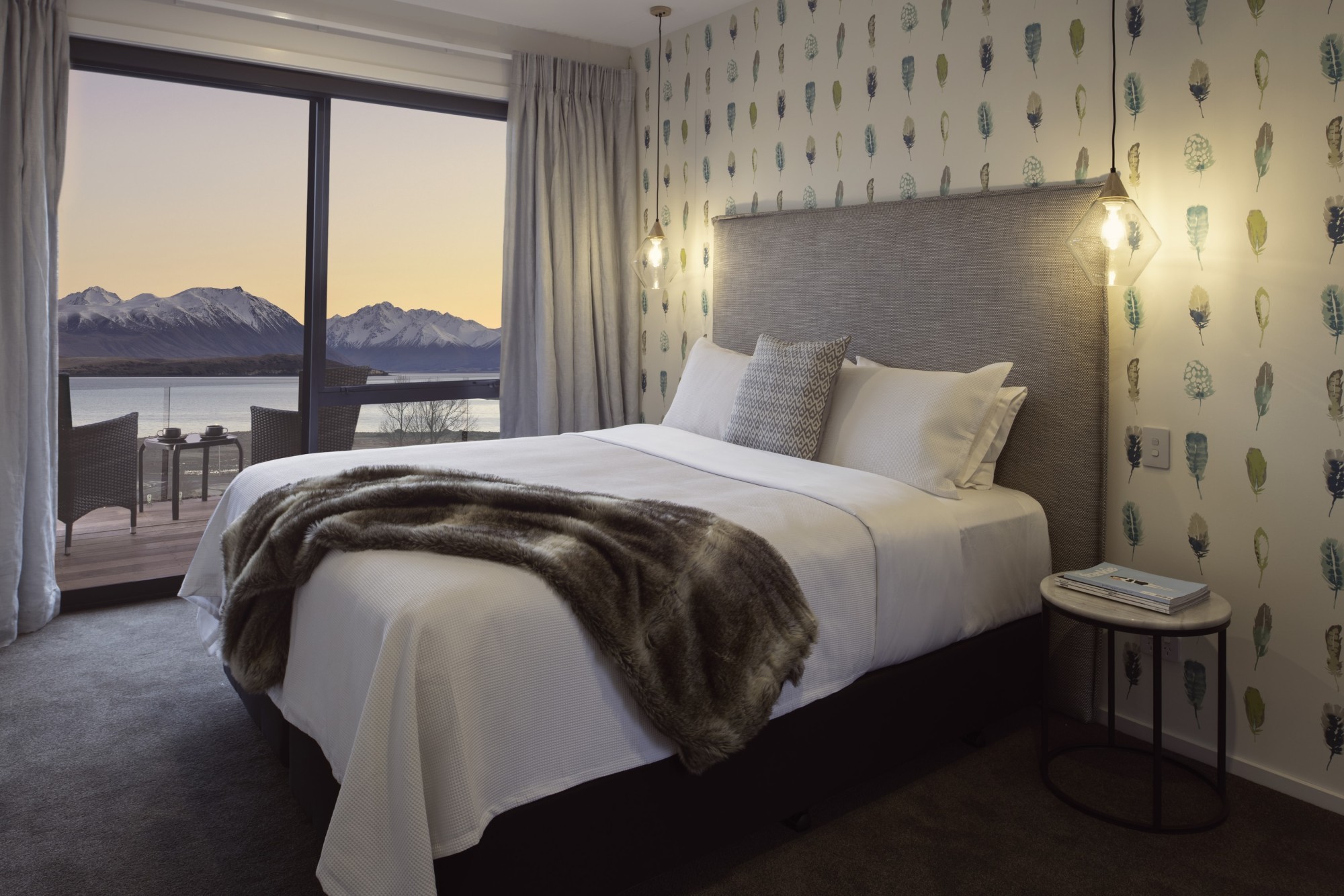 Stilvolles Bed-and-Breakfast-Zimmer in Neuseeland mit Kingsize-Bett, Feder-Tapete und Pelzdecke, mit einem privaten Balkon mit Blick auf einen See und schneebedeckte Berge bei Sonnenuntergang