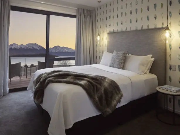 Stilvolles Bed-and-Breakfast-Zimmer in Neuseeland mit Kingsize-Bett, Feder-Tapete und Pelzdecke, mit einem privaten Balkon mit Blick auf einen See und schneebedeckte Berge bei Sonnenuntergang