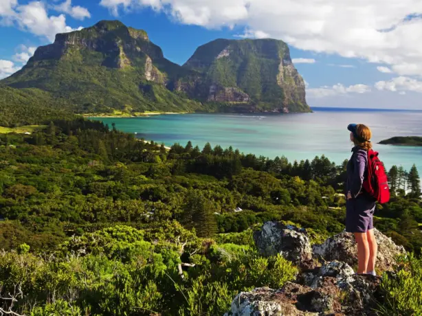 Eine wandernde Frau blickt auf das Meer und die Berge im Hintergrund