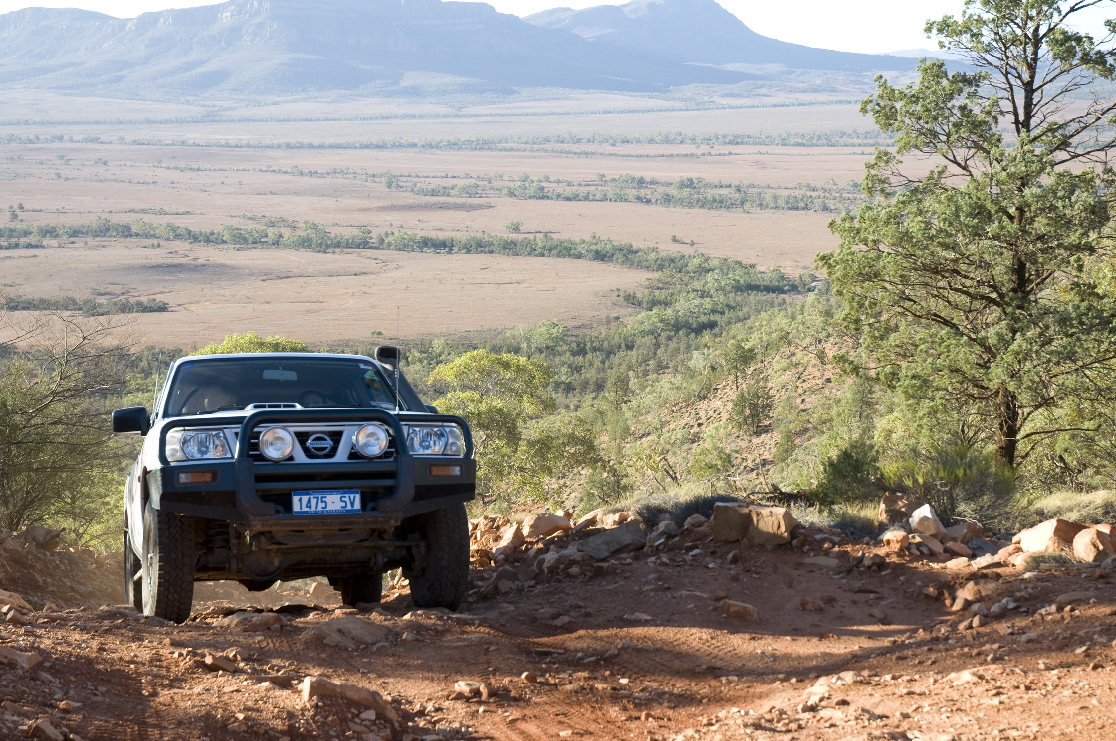 4WD car driving on an uphill dirt road with fields and mountains in the background