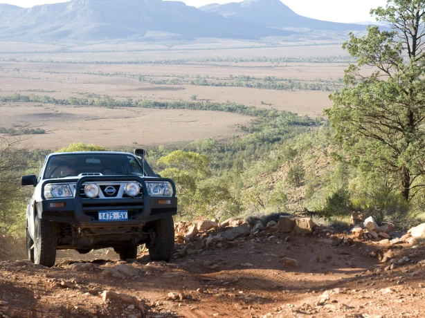 4WD car driving on an uphill dirt road with fields and mountains in the background