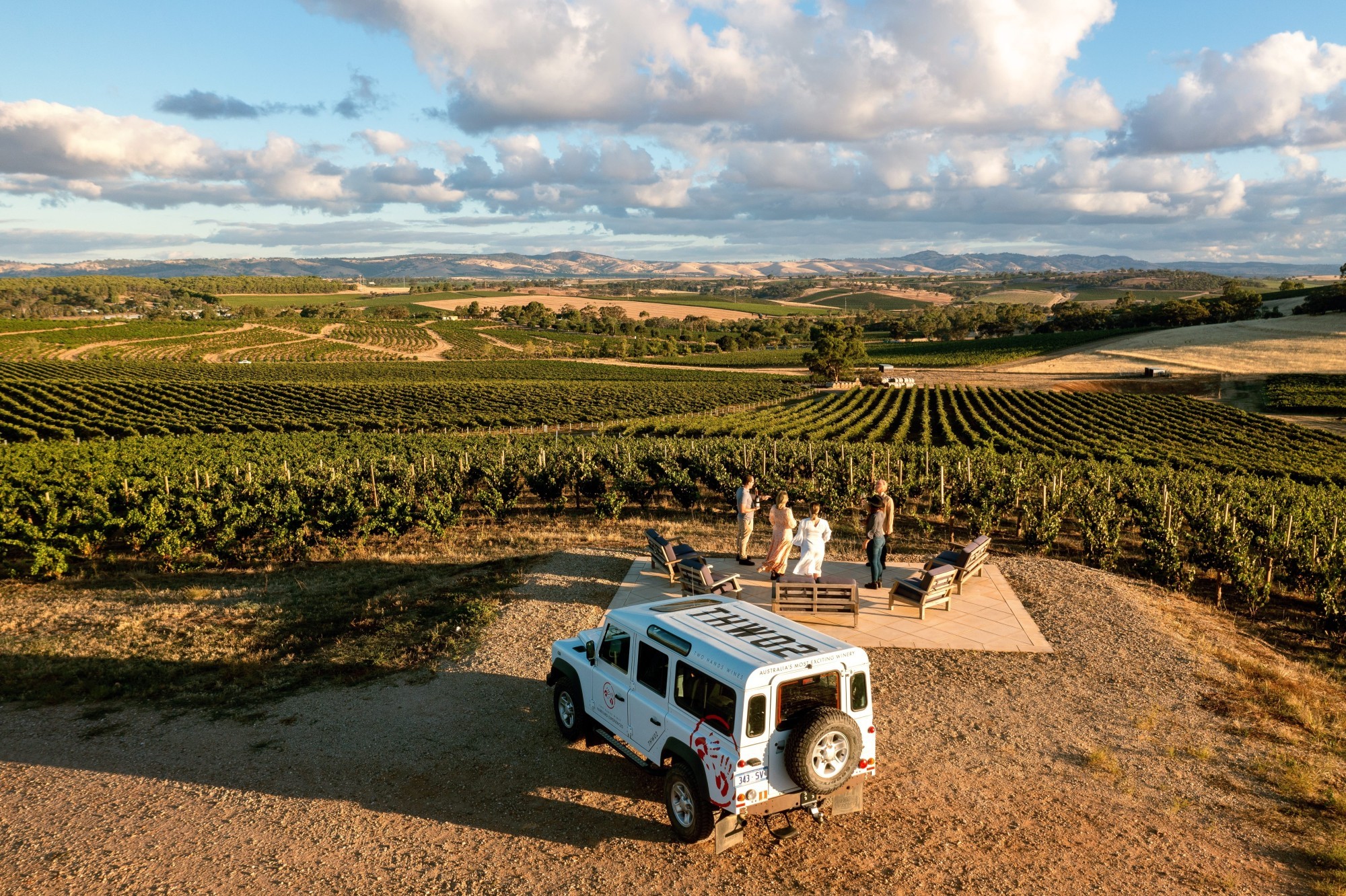 Menschen, die in einem Weinberg im Barossa Valley in Australien im Stehen etwas trinken.