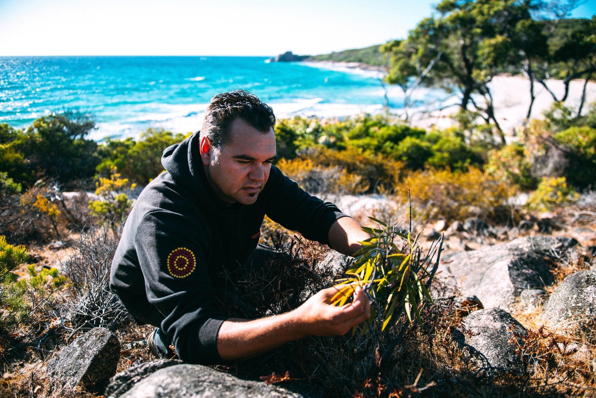 Indigener Guide betrachtet Pflanzen an Küste in Australien