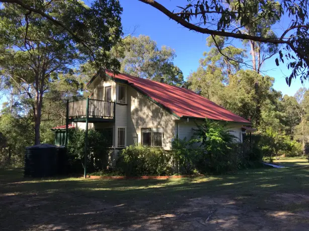 Freistehendes zweistöckiges Cottage mit rotem Blechdach und Balkon, umgeben von Eukalyptusbäumen und einer offenen Rasenfläche im australischen Busch an einem sonnigen Tag