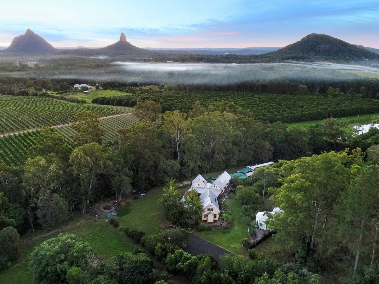 A lodge sits surrounded by greenery with Australia's Glasshouse Mountains in the background
