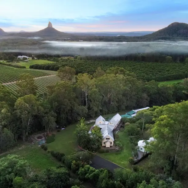 A lodge sits surrounded by greenery with Australia's Glasshouse Mountains in the background