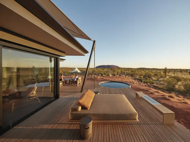 Luxuriöse Lodge-Terrasse mit Tagesbett und Tauchbecken mit Blick auf die rote Wüstenlandschaft von Uluru im Northern Territory Australiens, mit einem Paar im Hintergrund, das in der goldenen Stunde sitzt.