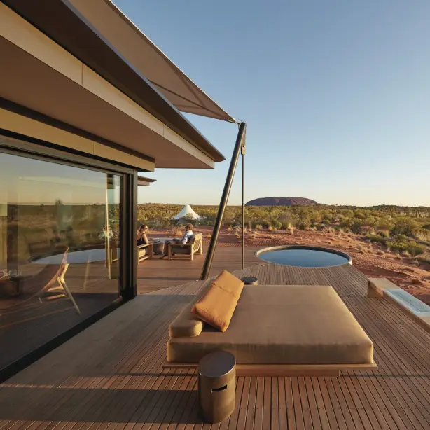Luxury lodge deck with daybed and plunge pool overlooking the red desert landscape of Uluru in Australia's Northern Territory, with a couple seated in the background at golden hour