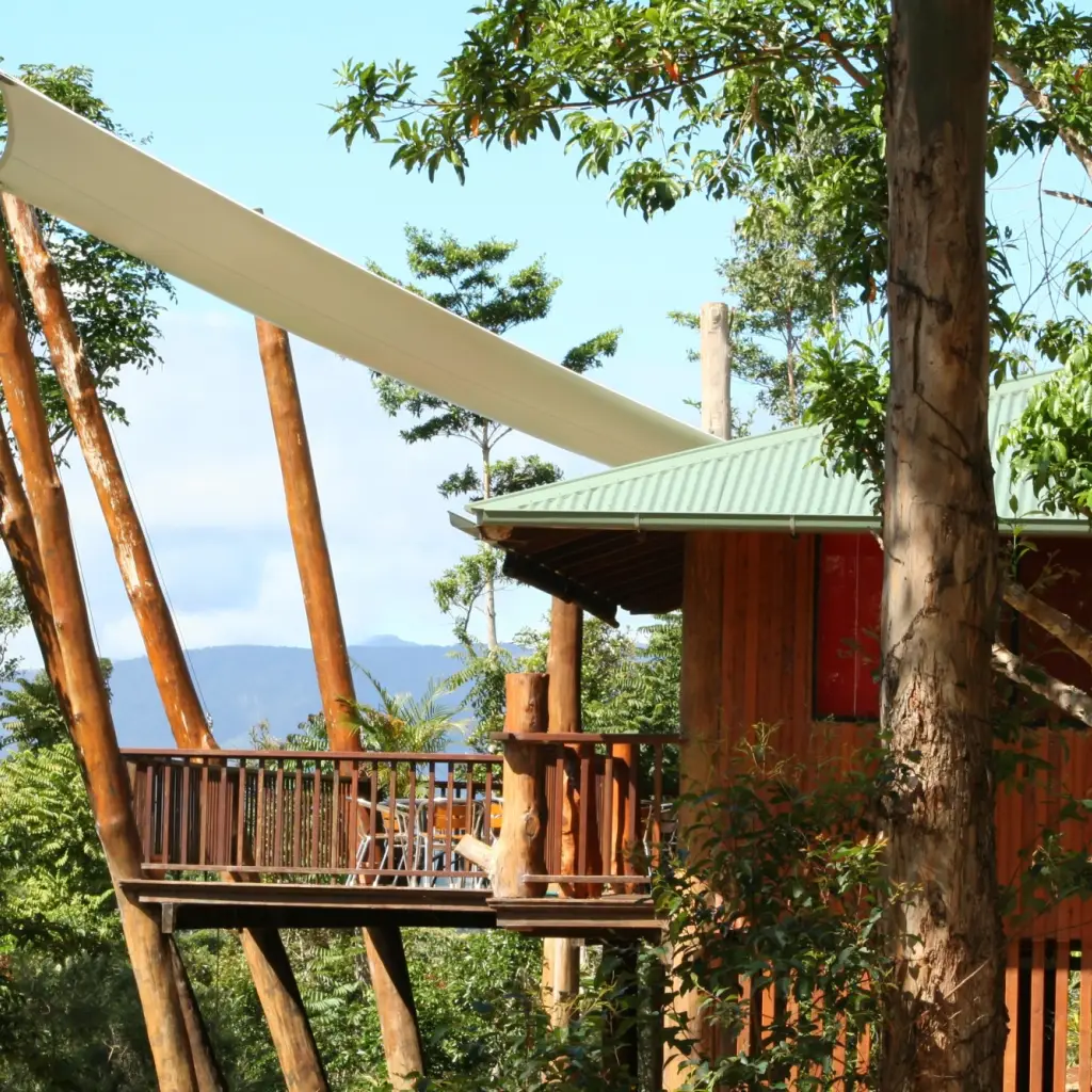 Erhöhtes Baumhaus mit umlaufender Terrasse und Sonnensegel, eingebettet zwischen üppigen Regenwäldern mit Bergblick, einzigartige Öko-Unterkunft in Australien