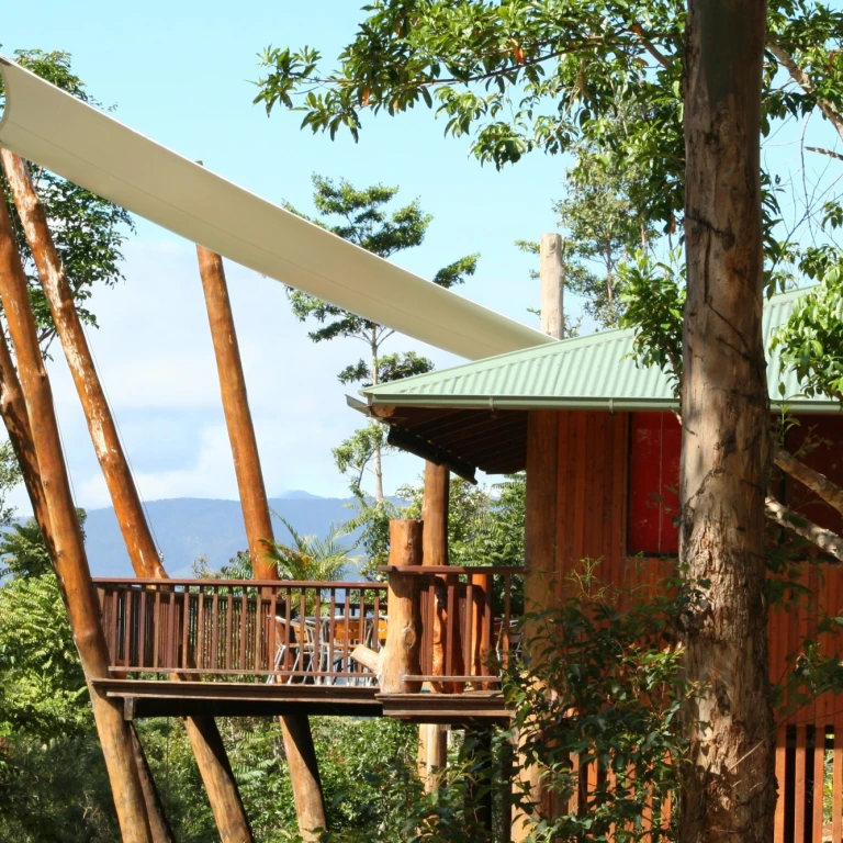 Erhöhtes Baumhaus mit umlaufender Terrasse und Sonnensegel, eingebettet zwischen üppigen Regenwäldern mit Bergblick, einzigartige Öko-Unterkunft in Australien
