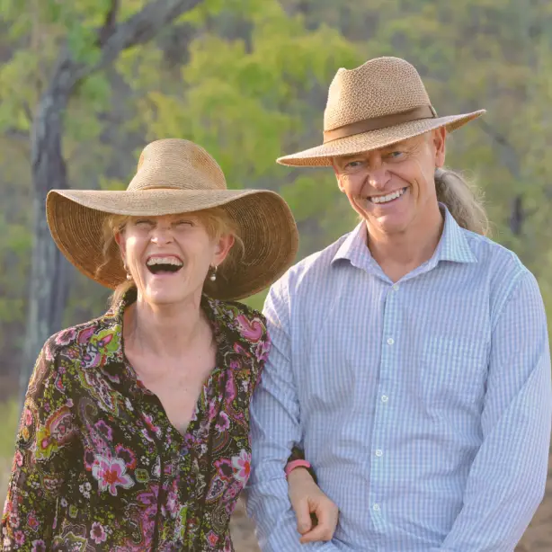 Ein lächelndes Paar mit breitkrempigen Hüten im australischen Outback von Queensland; Gastgeber eines lokalen Farmaufenthalts heißen ihre Gäste in ländlicher Buschlandschaft willkommen