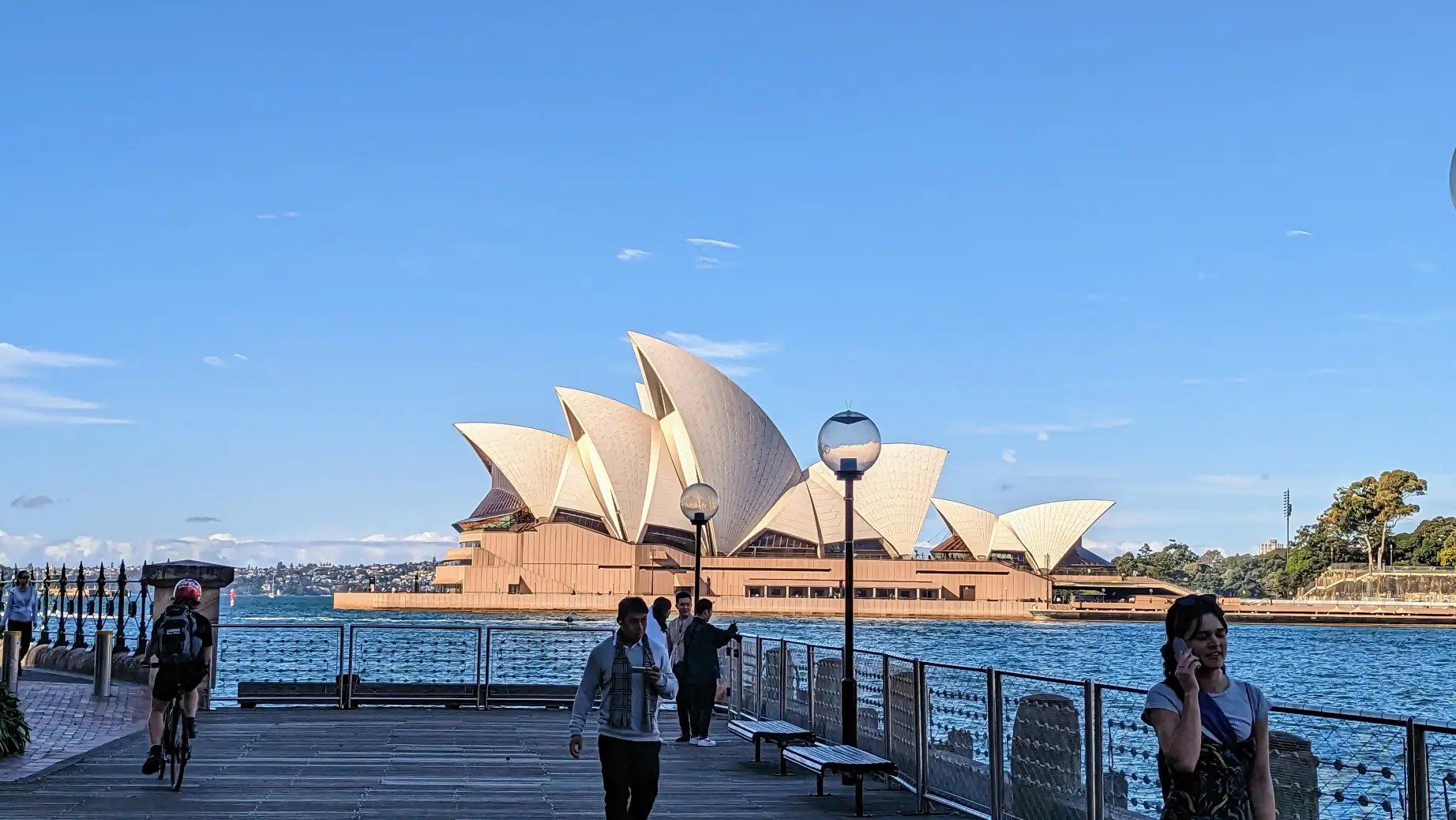 Blick auf das Opernhaus von Sydney von einem Steg aus, auf dem Menschen spazieren gehen