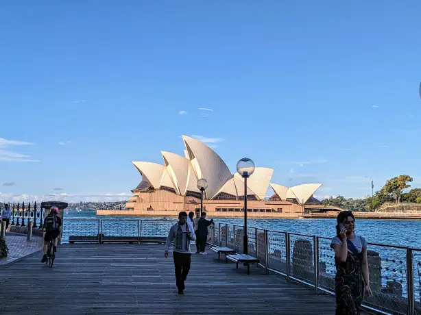 A view of the Sydney Opera House from a pier where people are walking
