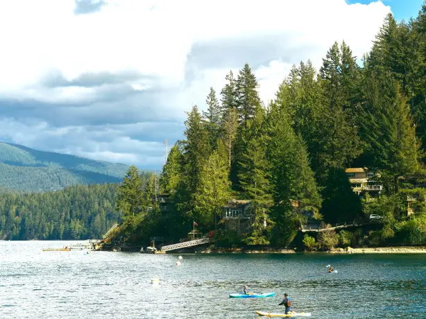 Ein ruhiger See mit bewaldetem Ufer und Kayak-Fahrern in Vancouver, Kanada