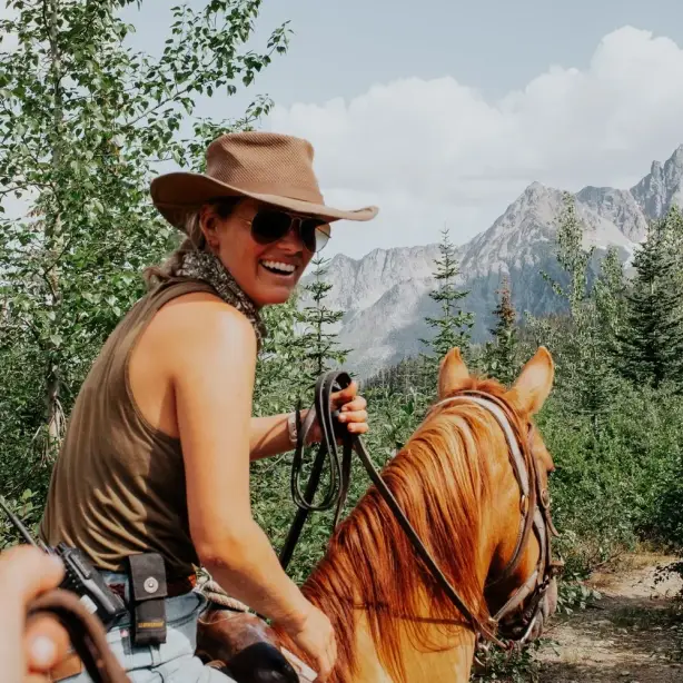 A local guide rides a horse and smiles back at the camera with mountains and trees in the background