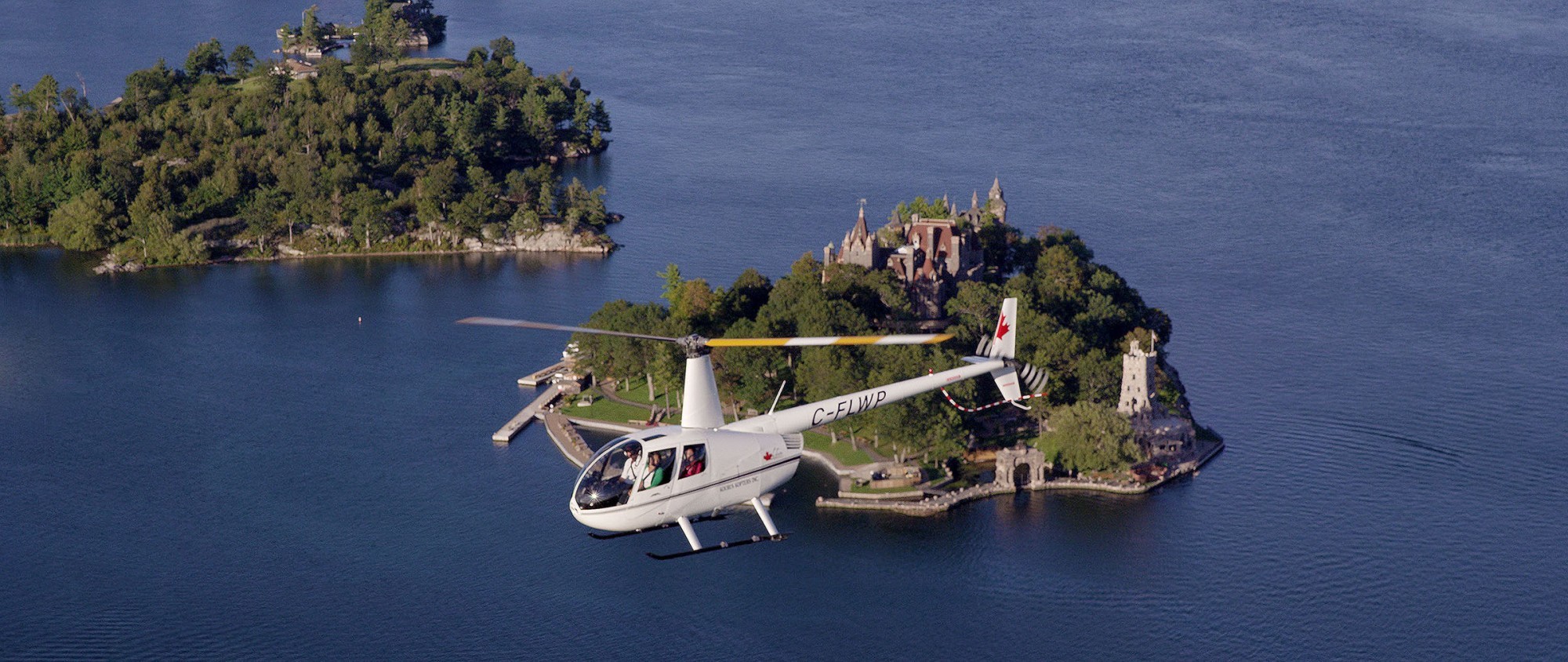 View of a white helicopter flying with passengers of an island with a castle in the Thousand Island, Eastern Canada