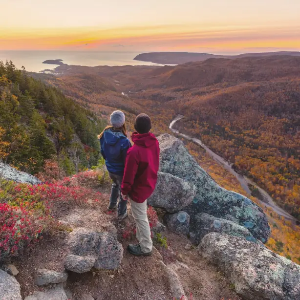 Zwei Wanderer stehen auf Felsen und blicken über herbstliches Flusstal