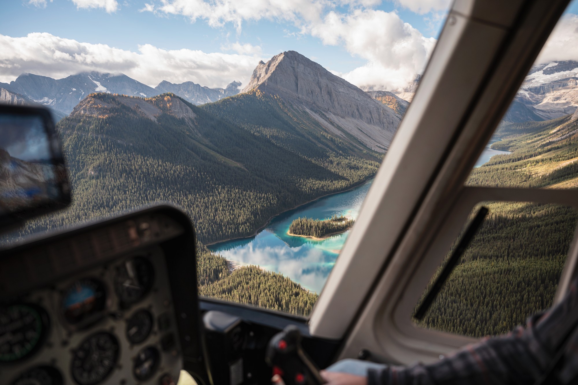 A pilot's view out the helicopter window of the Canadian Rockies with turquoise lakes and forested mountainsides