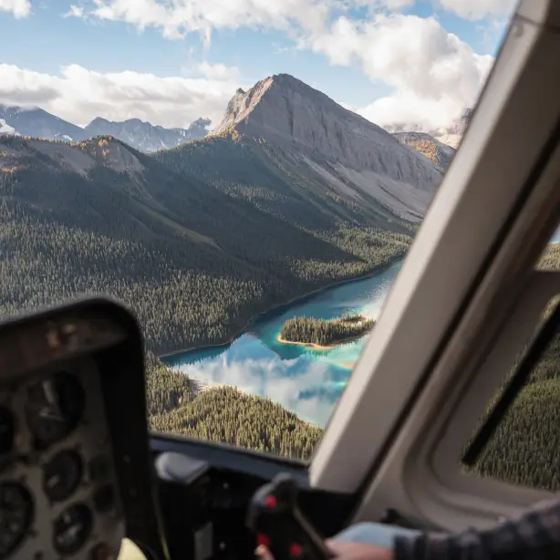 A pilot's view out the helicopter window of the Canadian Rockies with turquoise lakes and forested mountainsides