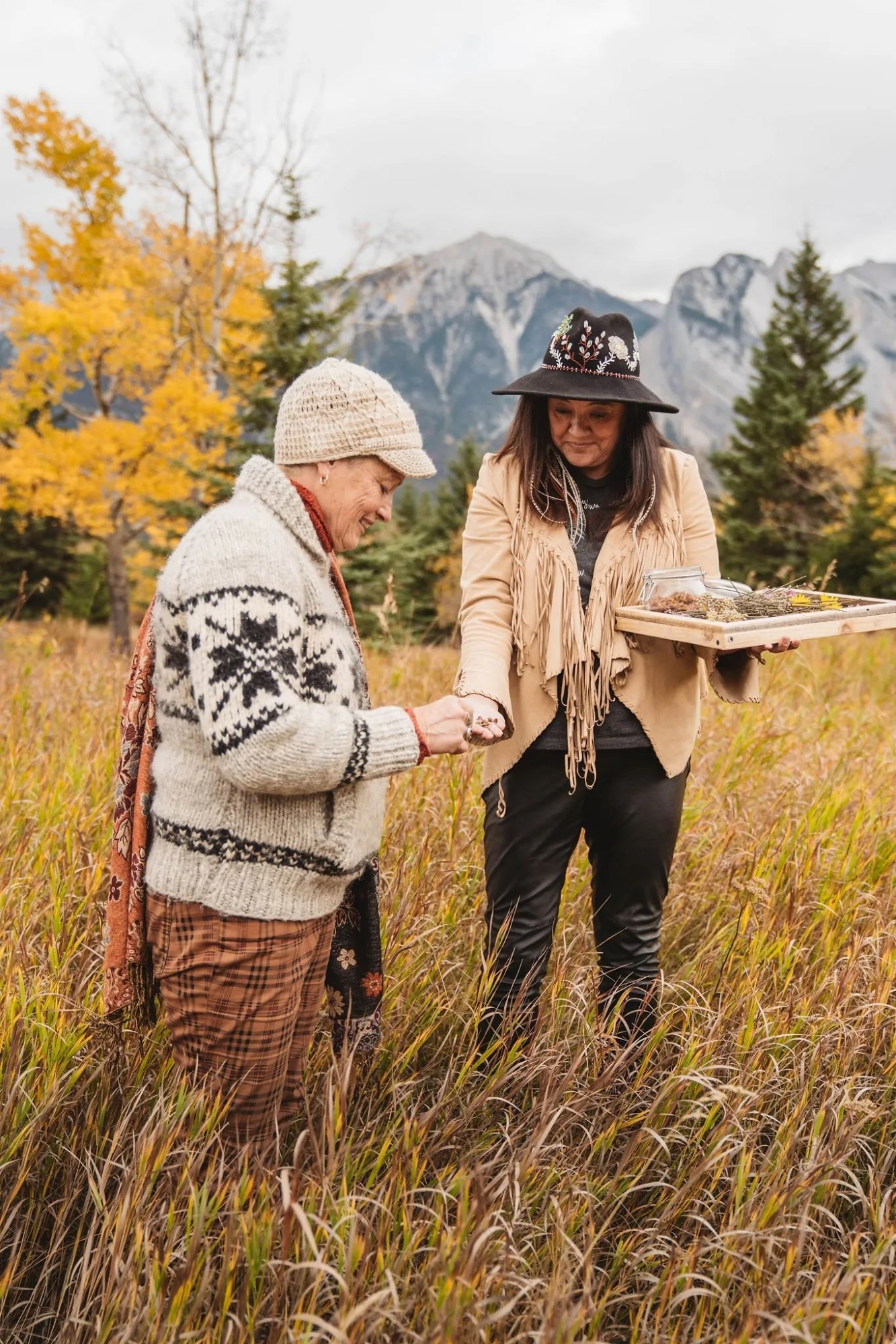 Indigenous female guide shows a woman medicinal herbs in a meadow.