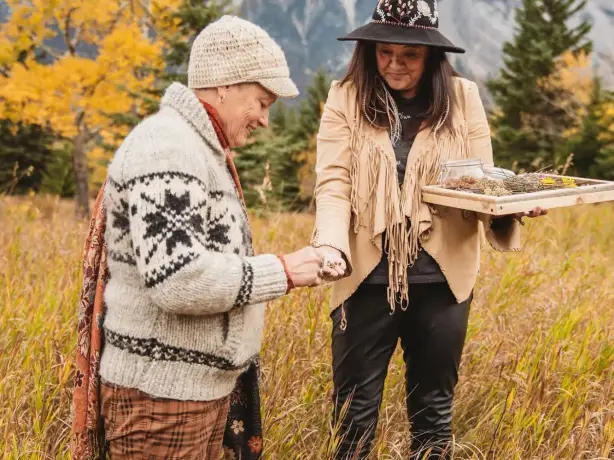 Indigenous female guide shows a woman medicinal herbs in a meadow.