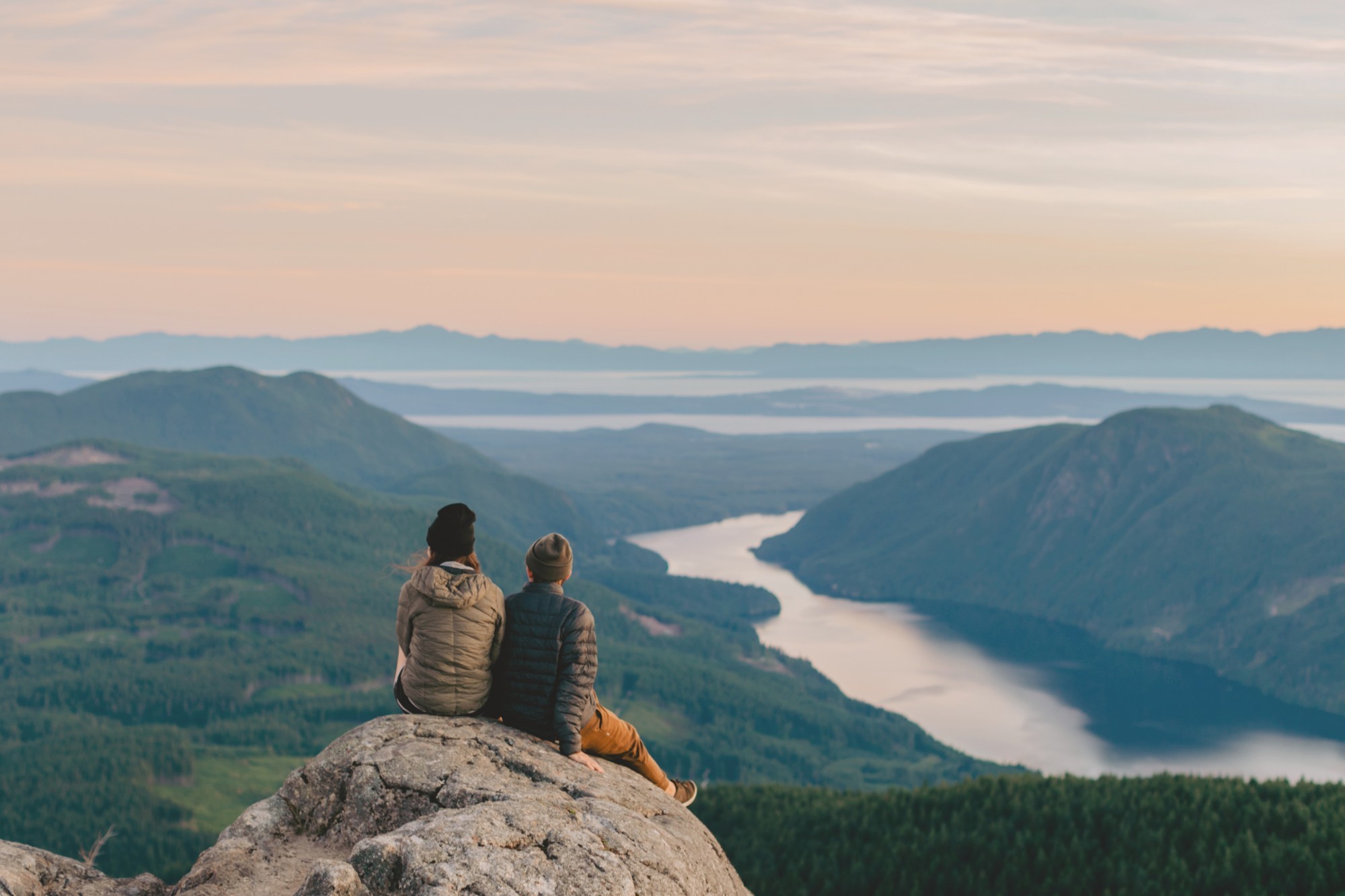 A couple sitting on a rock looking out towards the mountains and lakes, Sunshine Coast