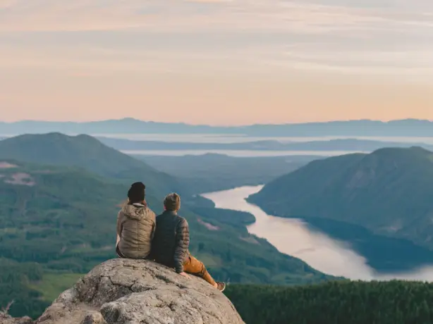 A couple sitting on a rock looking out towards the mountains and lakes, Sunshine Coast