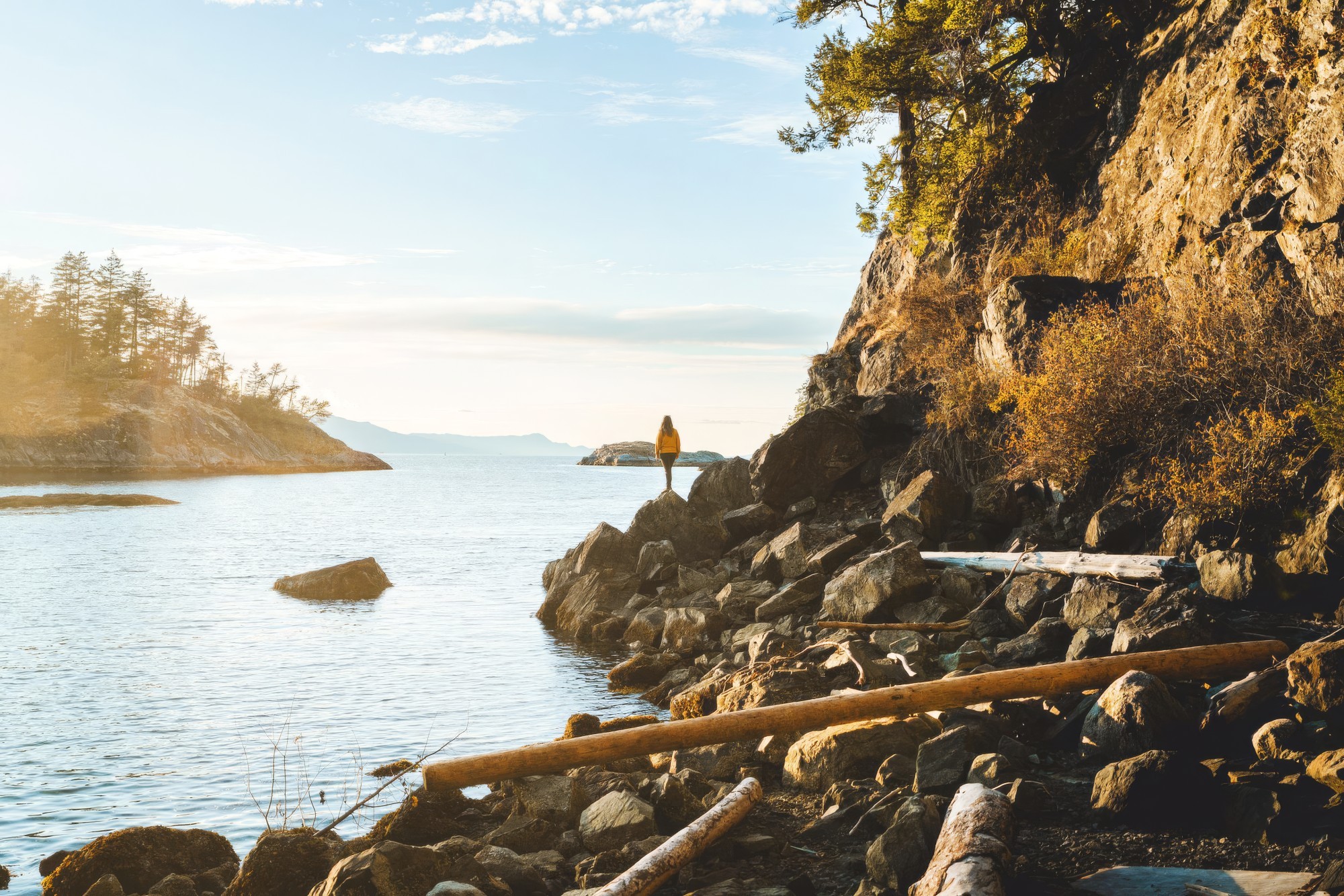 A woman standing at the edge of a rocky shoreline looking out at the view in Sunshine Coast