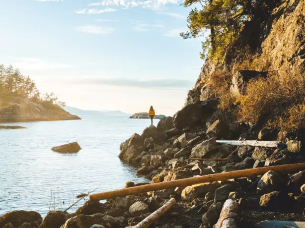 A woman standing at the edge of a rocky shoreline looking out at the view in Sunshine Coast