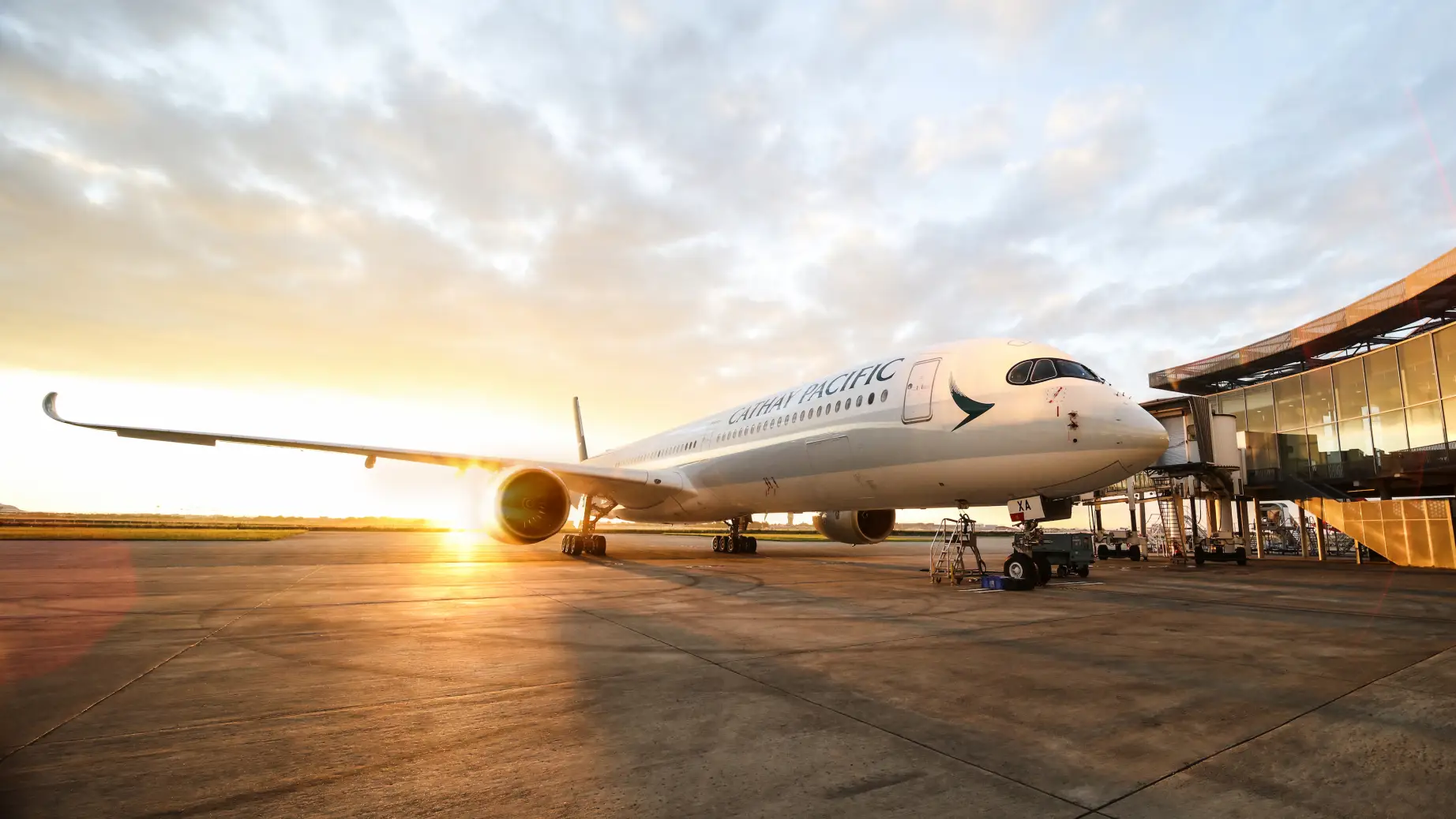 Ein Cathay Pacific Airbus am Flughafen mit einem Sonnenuntergang im Hintergrund.